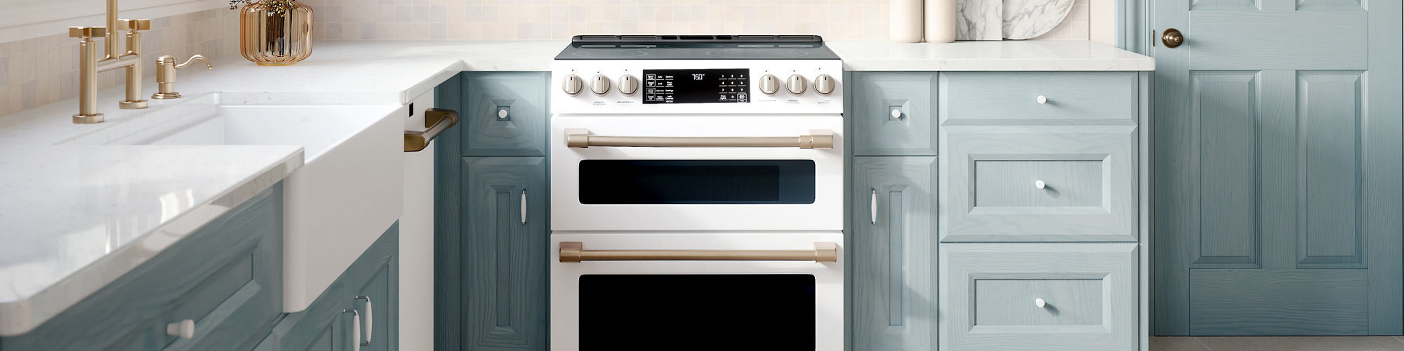 A bright, airy kitchen features light blue shaker-style cabinets and a white farmhouse sink. A white range and built-in microwave sit centered between the cabinets, creating a clean focal point. Sunlight streams through a large window, illuminating t