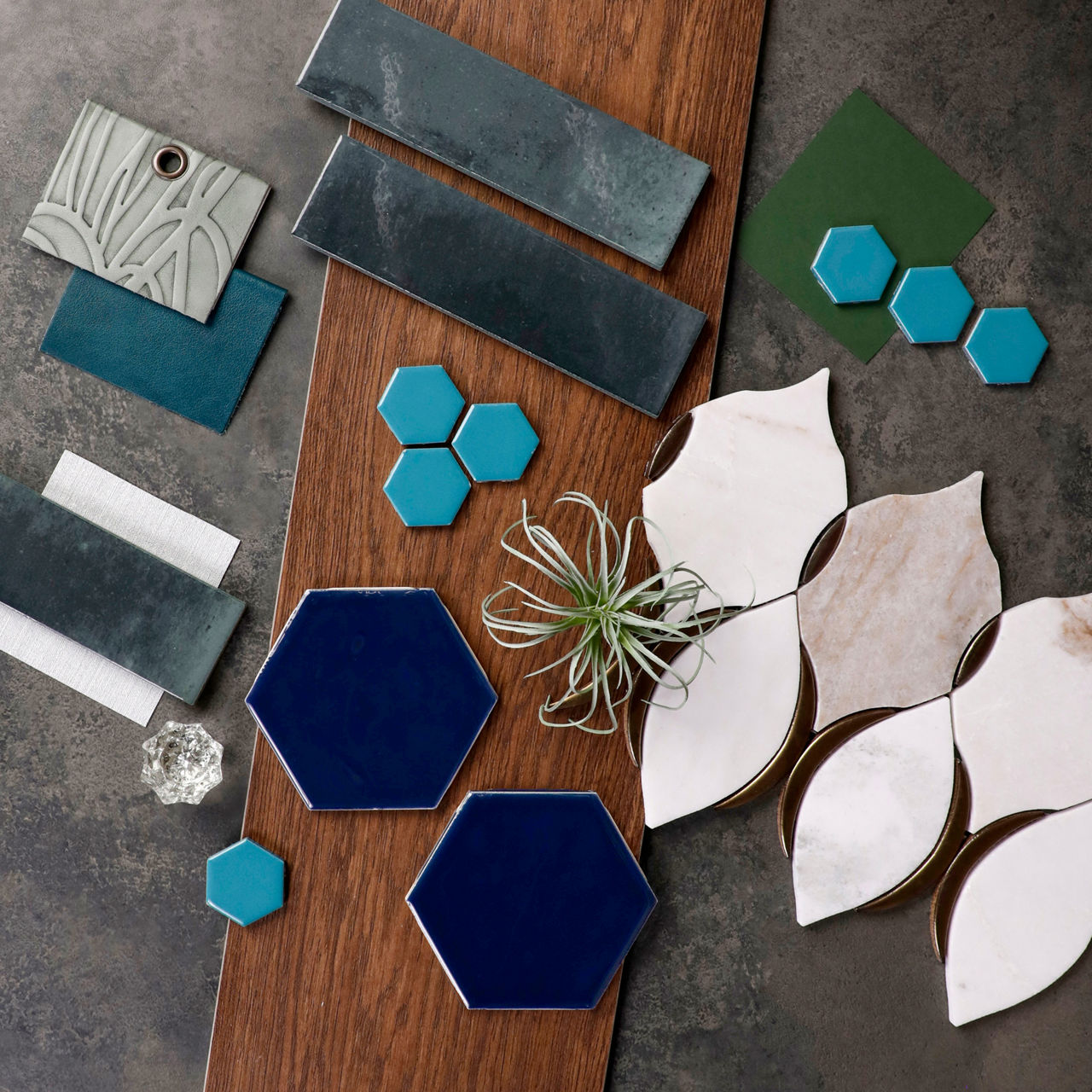 Tile flatlay featuring deep blue hexagon tiles, green rectangular tiles, and white leaf-shaped tiles arranged on a wood surface.