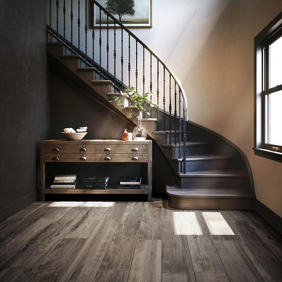 Dark wooden staircase with wood floors, wooden entrance table, and sun light shining through window.
