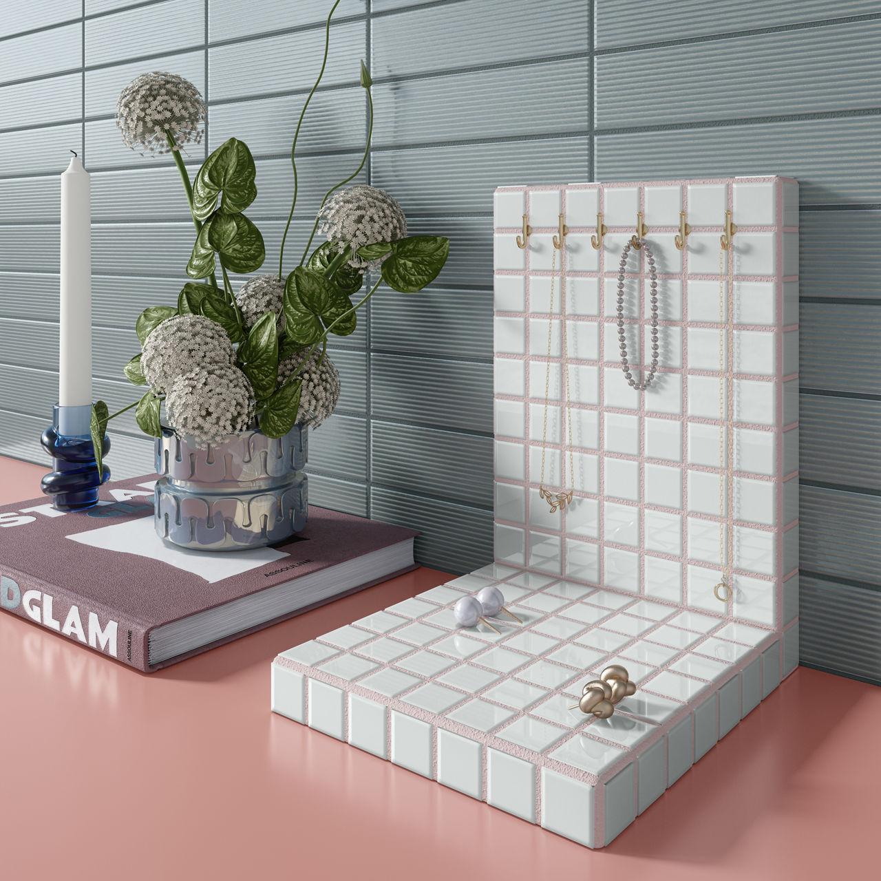 White square mosaic jewelry stand on a pink table, blue rectangle tile on back wall, and a book with a candle and plant on top.