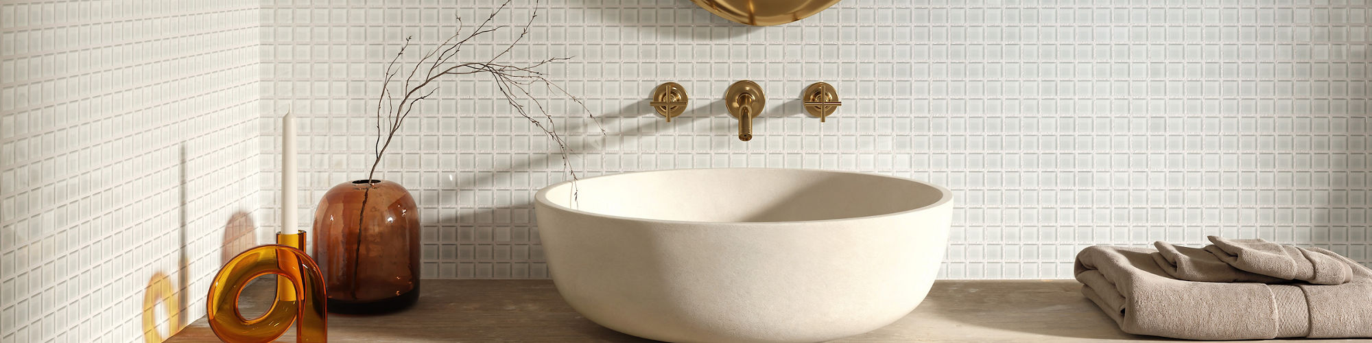 Bathroom with white square mosaic on walls, beige counter, white sink, and gold mirror above sink.