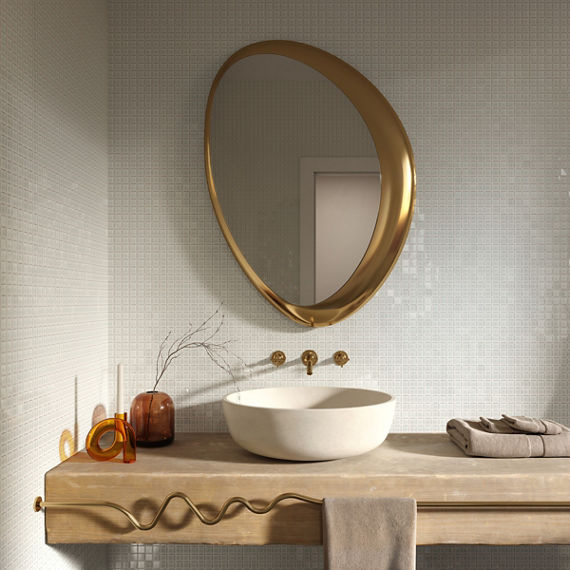 Bathroom with white square mosaic on walls, beige counter, white sink, and gold mirror above sink.