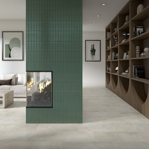 Living room with white rectangle floor tile, wooden bookshelf on wall, white couch, and fireplace with green subway tile on fireplace wall.