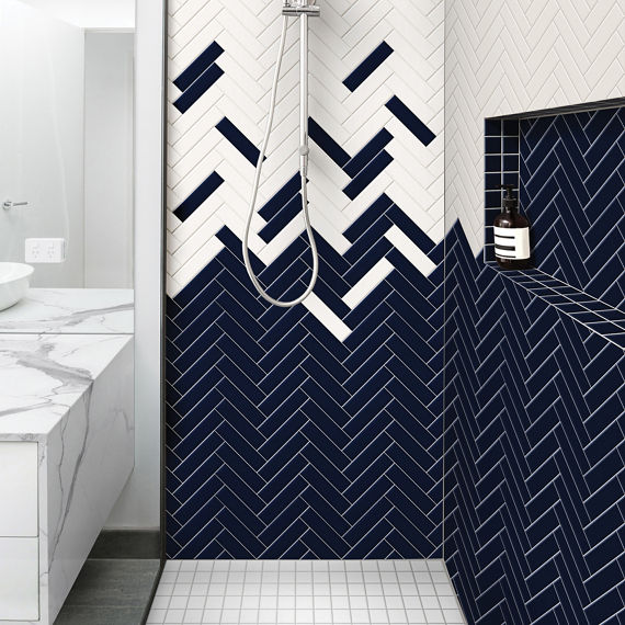 Bathroom shower with navy rectangle subway tile on shower wall, white rectangle subway tile on shower wall, white square mosaic tile on shower floor, and silver accents.