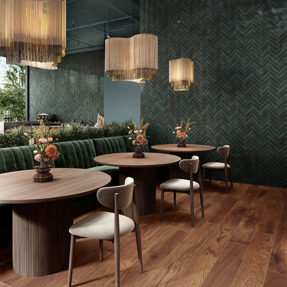 Restaurant with blue rectangle subway tile on walls in herringbone pattern, wood look floor tile, round wooden tables, green booths, and white chairs.