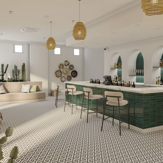 Cafe with white walls, black and white penny round mosaic tile on floor in diamond pattern, beige couch, bar with green subway tile on surround, white marble look countertop on bar, and white bar chairs.