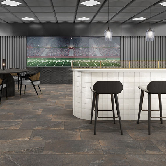Stadium lounge with brown stone look rectangle floor tile, white bar, two black bar chairs, and a football field in the background.