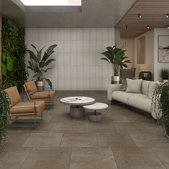 Waiting area with gray square stone look floor tile, white rectangle concrete look wall tile on back wall. greenery on side wall, white couch, and two tan chairs.