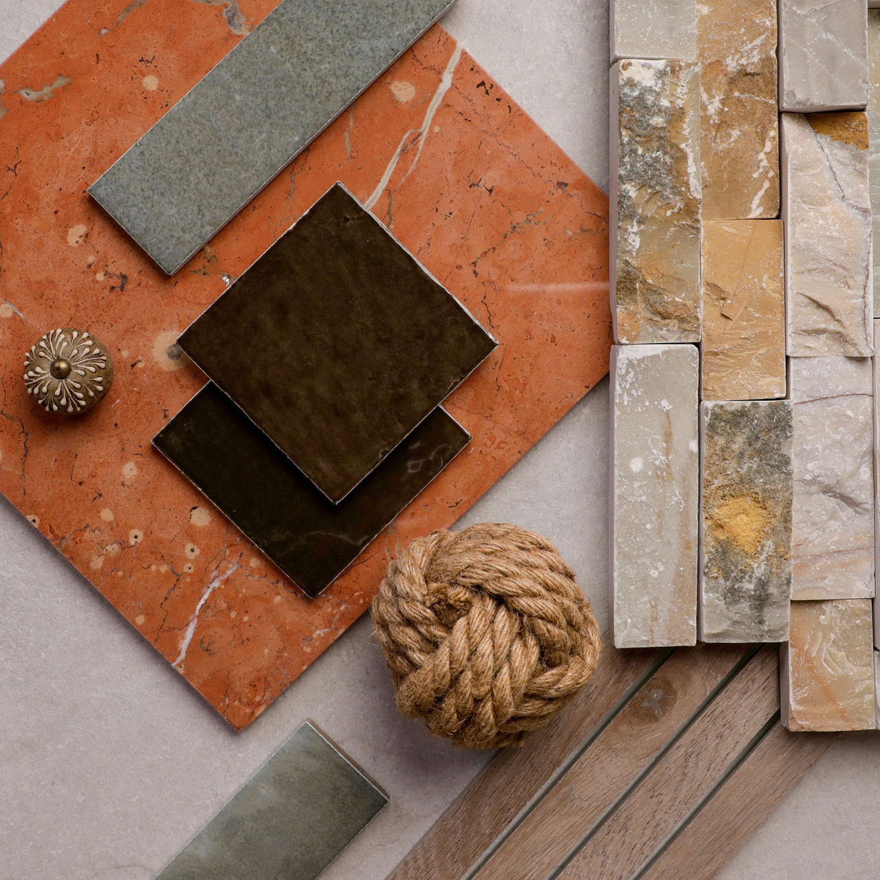 Tile flatlay with warm earth-toned rectangular tiles, gray stone-look pieces, and a black square tile on a rust-colored background.