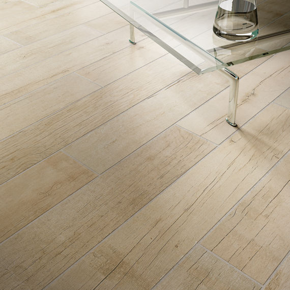 Close up of wood look floor tile, glass table,  and pitcher of water on table.