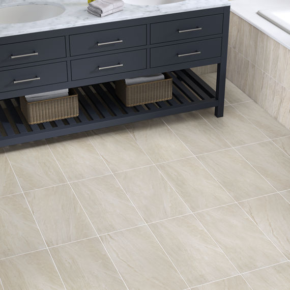 Close up of bathroom with navy cabinets, white marble look countertop, silver accents, and light beige stone look rectangle floor tile.