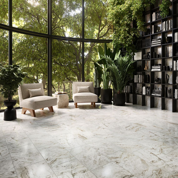 Library with large windows on wall, bookshelf with books and vases, two white sitting chairs, greenery outside windows, plants in black vases, and white rectangle marble look floor tile.