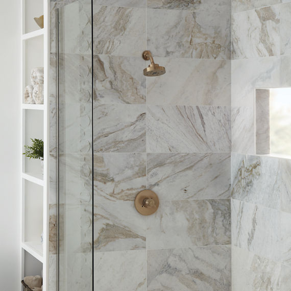Stand up shower with white rectangle marble look tile on shower walls, white pebble look tile on shower floor, and gold accents.