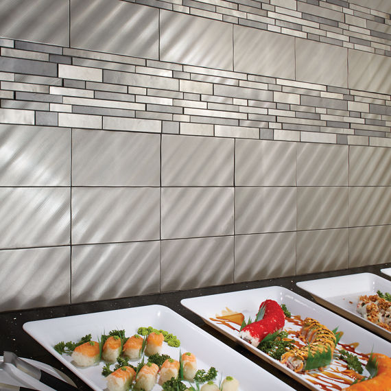 Sushi bar with white plates, sushi arranged in rows, and a silver metal backsplash.
