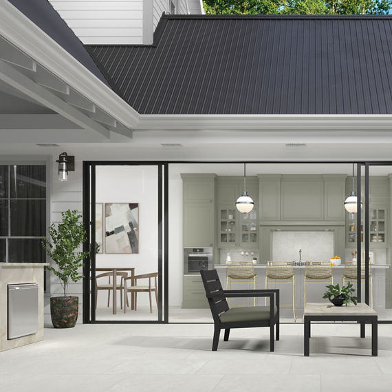 Outdoor dining area with white stone look rectangle floor tile, white walls, black furniture, sliding glass doors showing inside kitchen, and small plant.
