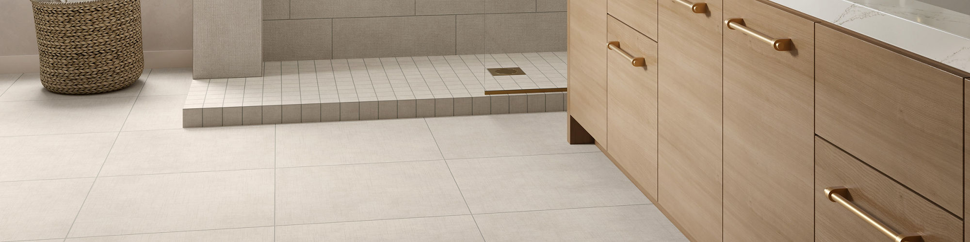 A spacious contemporary bathroom features a large walk-in shower with a built-in bench. Light beige tiles cover the floor and walls, creating a clean and cohesive look. A wooden vanity with gold hardware and a white countertop runs along one side, to