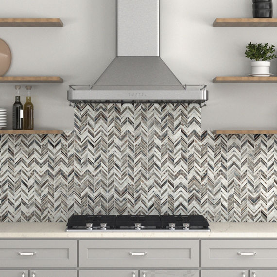 Kitchen with stone look gray herringbone mosaic on backsplash, floating wooden shelves, light gray cabinets, and a white countertop.