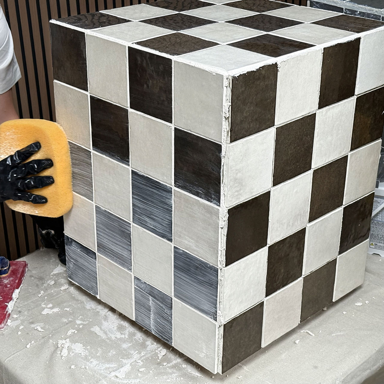 White and brown checkered square tile table with grout being pressed into spaces.