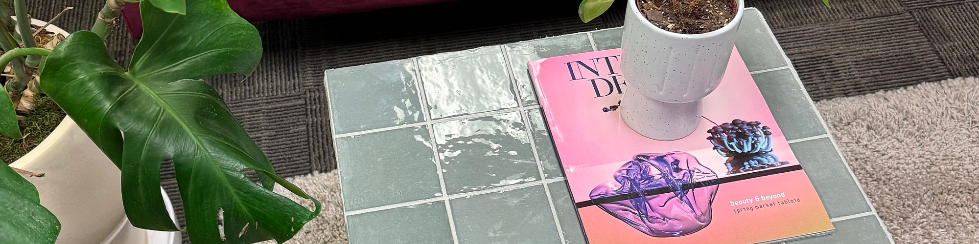 Gray square tiled table, pink couch, magazine on table, and small plant on table.