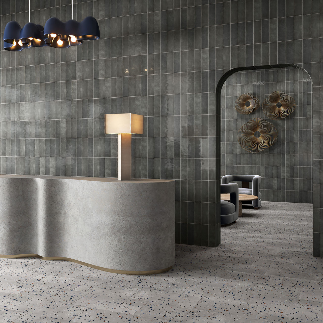 Waiting area with gray stone look rectangle wall tile in vertical pattern, gray speckled floor tile, gray welcome desk, and two gray chairs in the back.