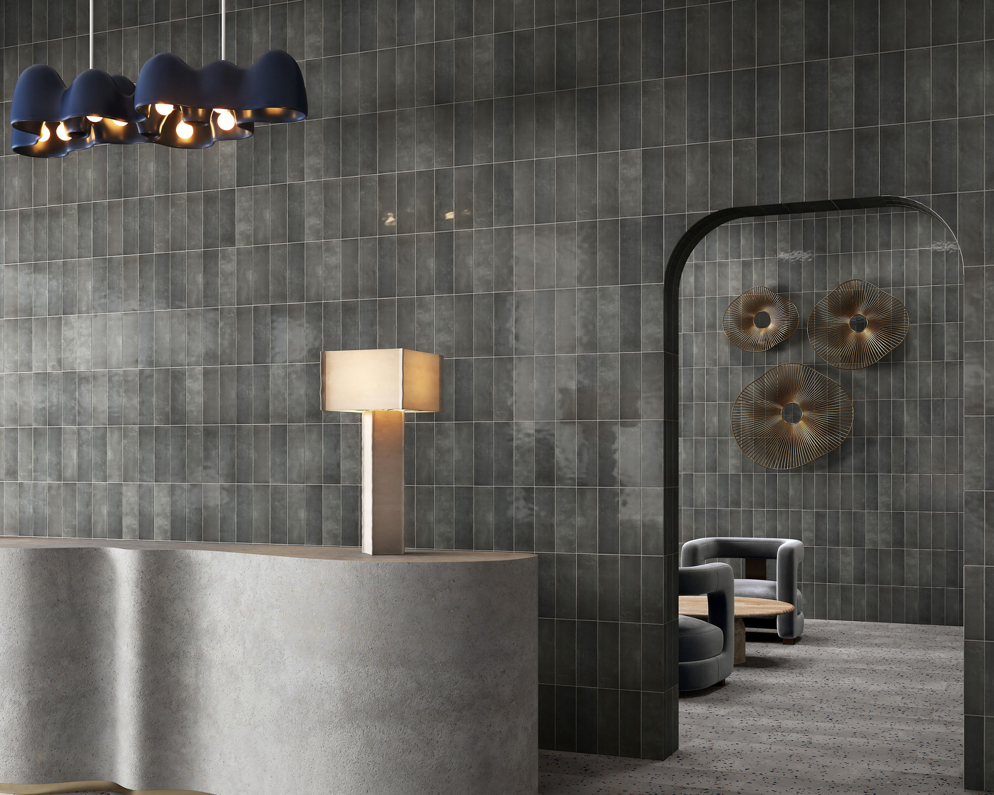 Waiting area with gray stone look rectangle wall tile in vertical pattern, gray speckled floor tile, gray welcome desk, and two gray chairs in the back.