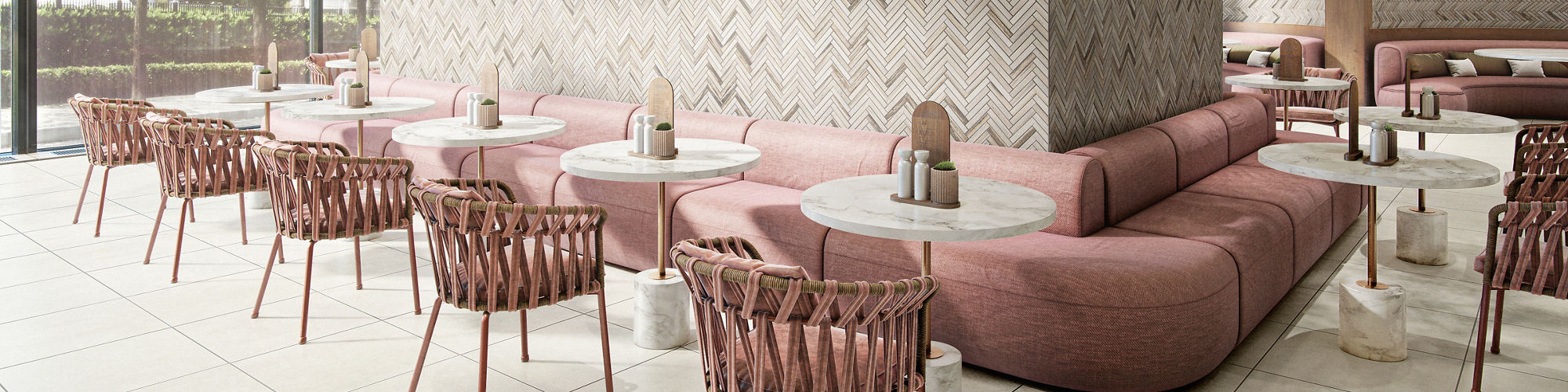 Restaurant with trees in center, pink couches surrounding trees, white concrete look square tile, wooden chairs with pink cushions, and a natural stone chevron mosaic on tree surround and back walls.