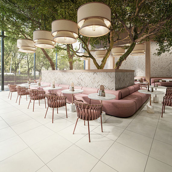Restaurant with trees in center, pink couches surrounding trees, white concrete look square tile, wooden chairs with pink cushions, and a natural stone chevron mosaic on tree surround and back walls.