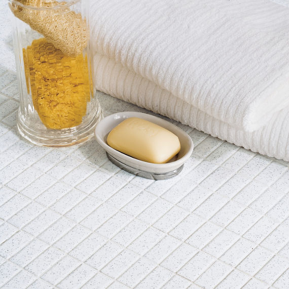 Close up of white rectangle tile in straight pattern, bar soap in bowl, white towels, and loofahs.