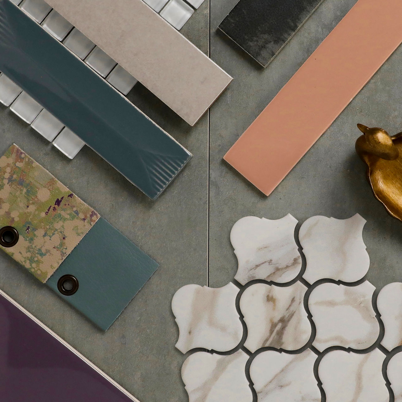 Tile flatlay featuring blush pink rectangular tiles, teal strips, and white quatrefoil tiles on a gray surface.