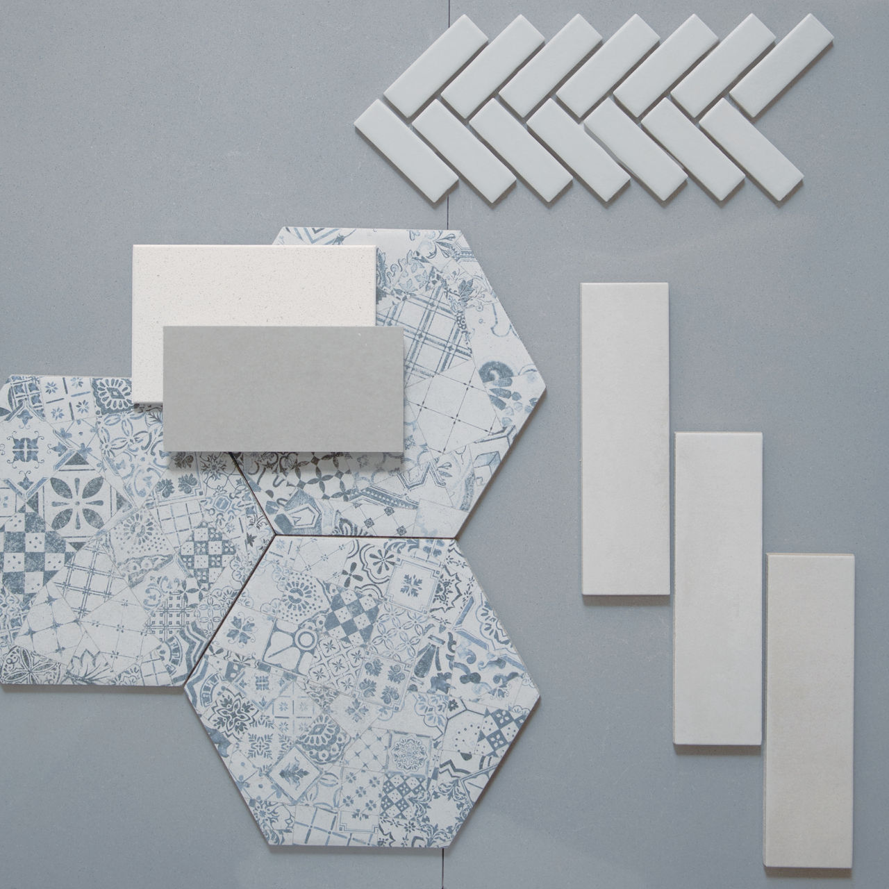This flatlay contains concrete look tile accented by concrete accent tile, herringbone mosaic, and encaustic hexagon tile.