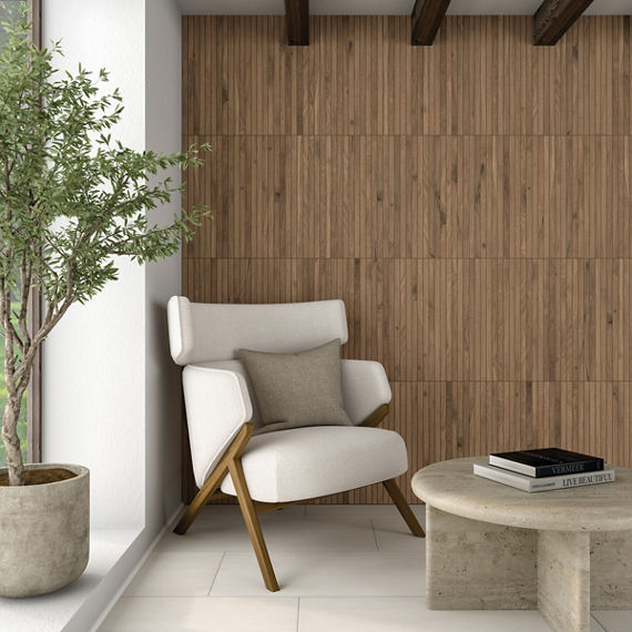 A contemporary white armchair with cushions sits beside a large potted tree in a bright corner of a room. The space features a wood-paneled accent wall and exposed ceiling beams, adding warmth and texture. In front of the chair is a round stone coffe