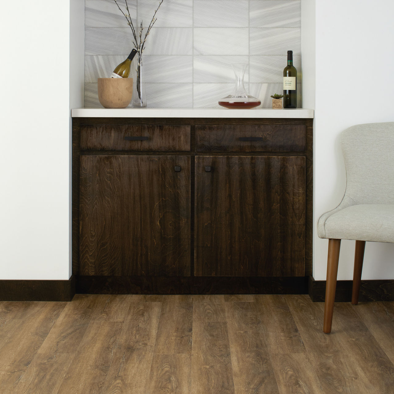 A contemporary home bar nook features dark wood cabinetry and a white countertop. 