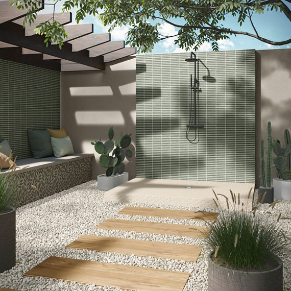 Outdoor shower with wood look floor tile creating a path, green rectangle mosaic tile on shower wall, gray side walls, and cacti throughout shower area.