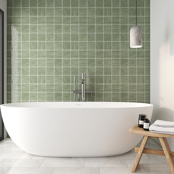 Bathroom with white bathtub, small wooden stool, and green square tile on back wall.