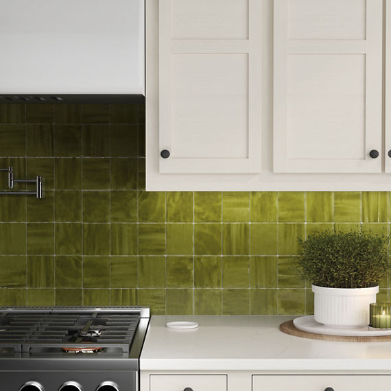 Kitchen with white cabinets, small plant, green candle, and green square tile on backsplash.