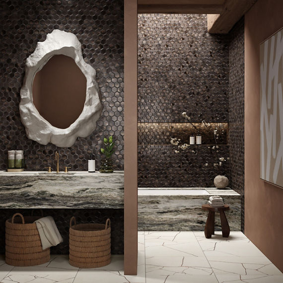 Bathroom with brown hexagon mosaic tile on walls, white rectangle floor tile, white quartz countertop and bathtub, and white round mirror above sink.