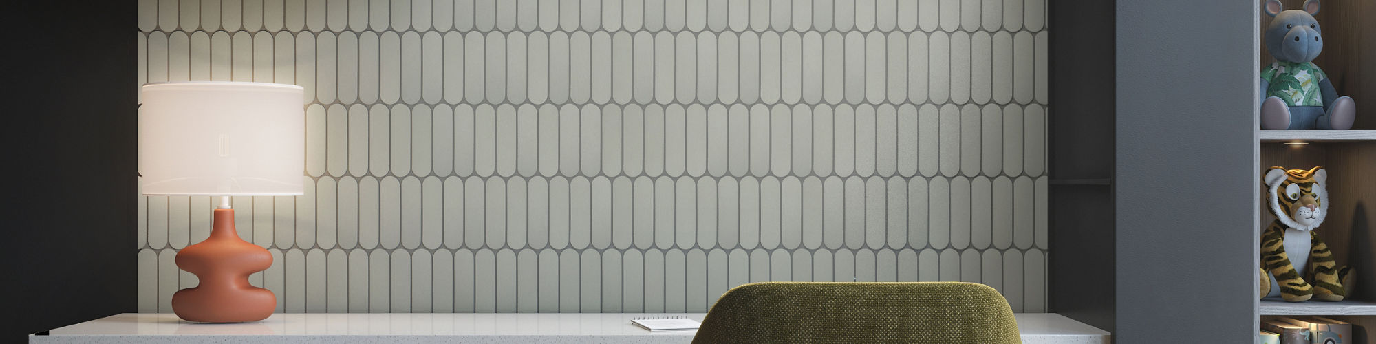 A contemporary home office workspace features a white desk with black drawers and a green upholstered chair. The wall behind the desk is covered in light patterned tiles, illuminated by a sleek overhead light. Open shelves above and to the side displ