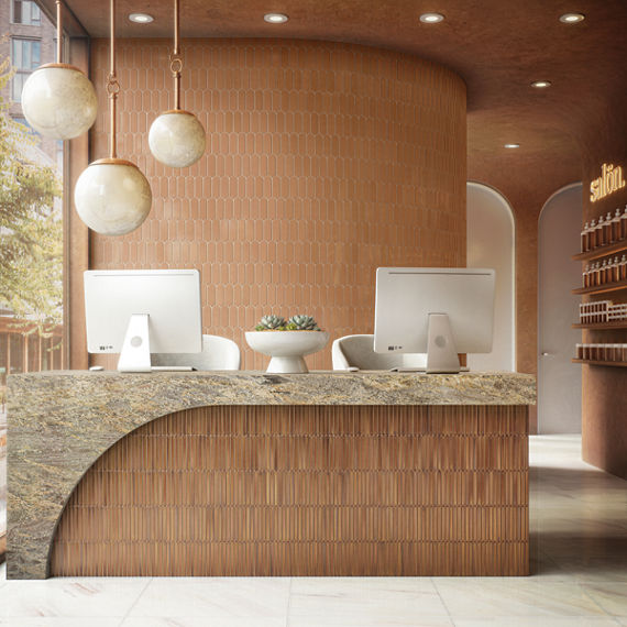 Front desk with orange fishscale mosaic tile on back wall, rectangle mosaic on counter wall, and a beige granite countertop.