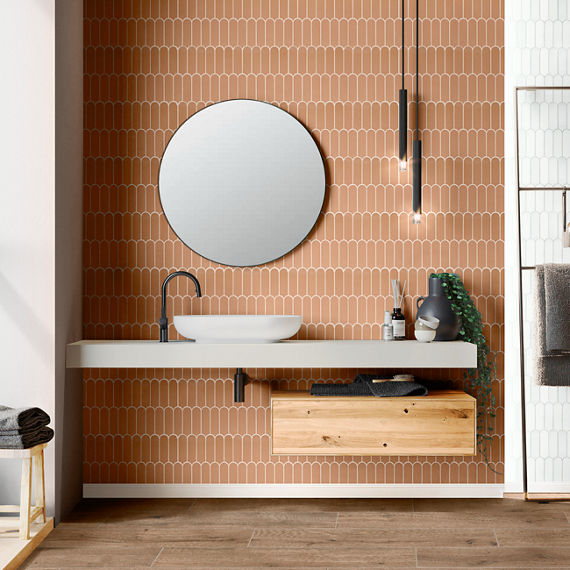 Bathroom with white countertop, round mirror, orange fishscale mosaic on back wall, and white fishscale mosaic on side walls.