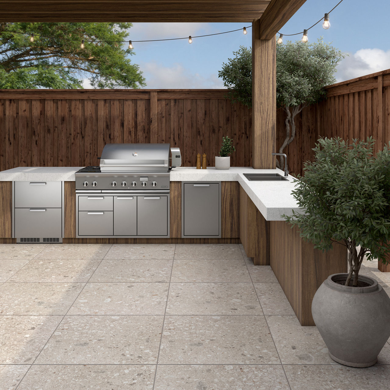 Outdoor kitchen with silver grill, wood cabinets, and white stone look pavers.