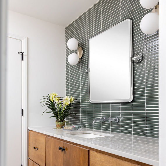 Bathroom with green rectangle tile on back wall, white quartz countertop, wood cabinets, and rectangle mirror above sink.