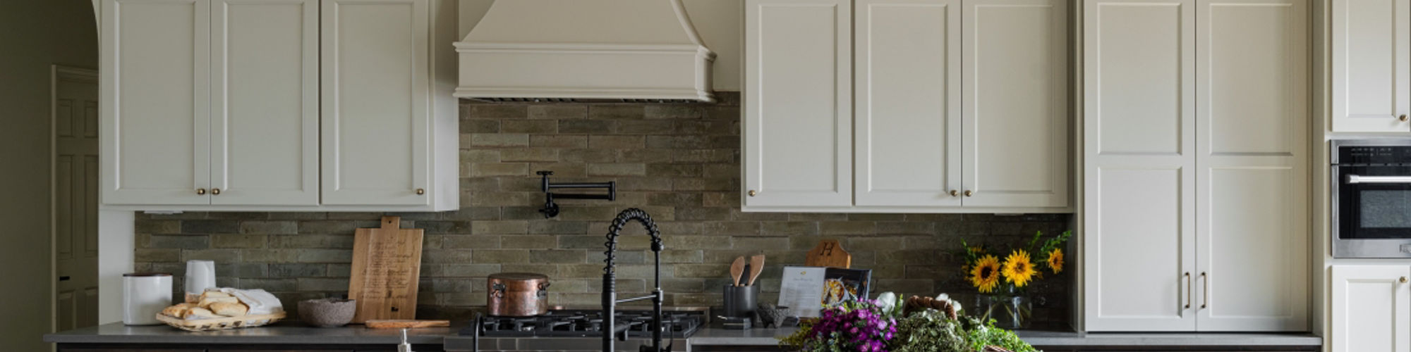 Renovated kitchen with off white cabinets, glossy brown subway tile backsplash, gray quartz countertops, island with sink and basket pendant lighting.