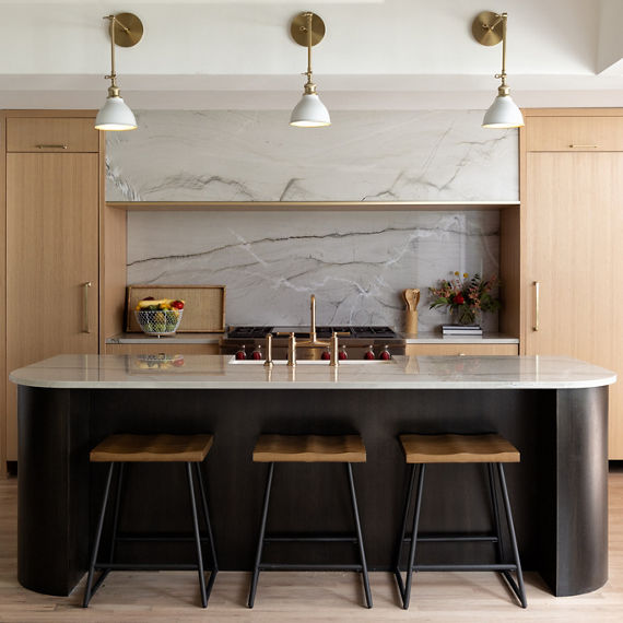 Kitchen with birch wood cabinets, dark wooden base and a gray veined quartzite countertop, backsplash and vent hood.
