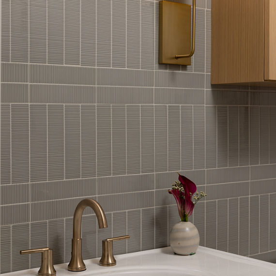 Bathroom with gray rectangle rippled wall tile in corridor pattern, white sink, small greenery on sink, and gold accents.