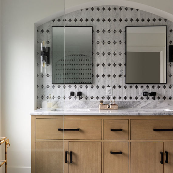 Bathroom with light brown wood cabinets on his and hers sinks, white marble floor, white marble look mosaic on wall, and white marble slab on the countertops.