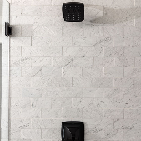 Shower with white marble rectangle tile in brick joint pattern on walls, black showerhead, and black wall faucet.