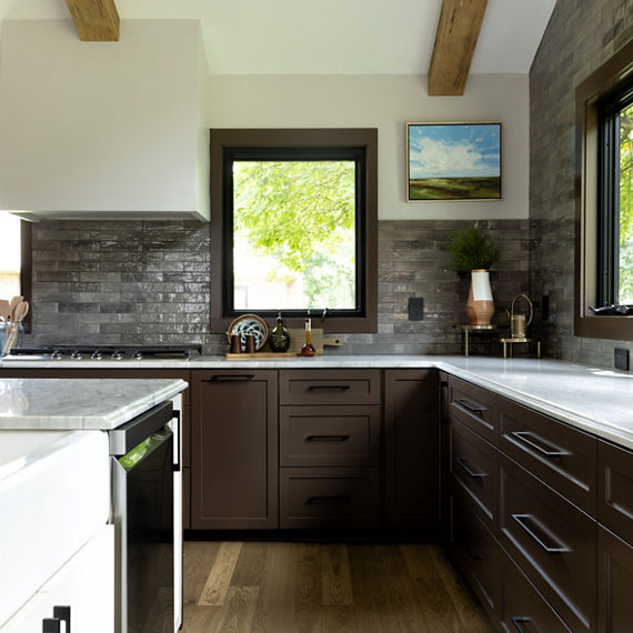 Kitchen with center island, brown cabinets, light wood floors, white quartzite slab countertop, and gray undulated subway tiles on the walls.