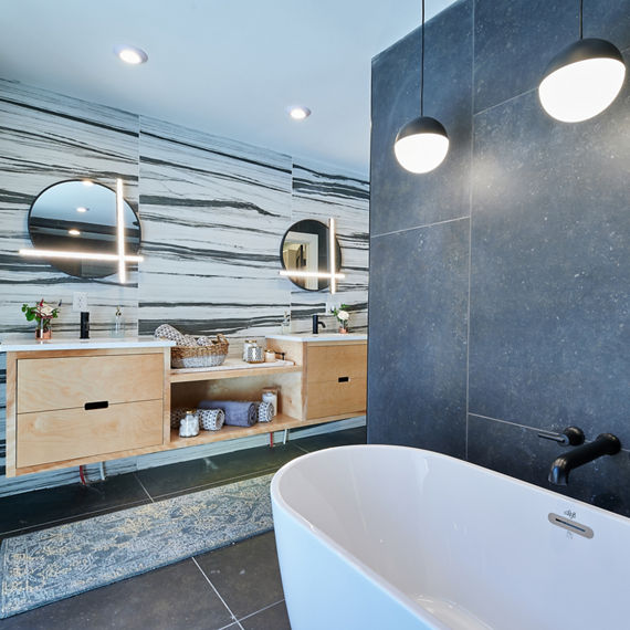 Bathroom with black and white stone look rectangle on back wall, gray stone look rectangle tile on side walls and floor, and white bathtub.