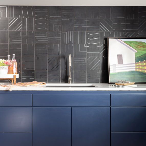 Kitchen with black metal look geometric square tile n backsplash, blue cabinets, and white countertop.