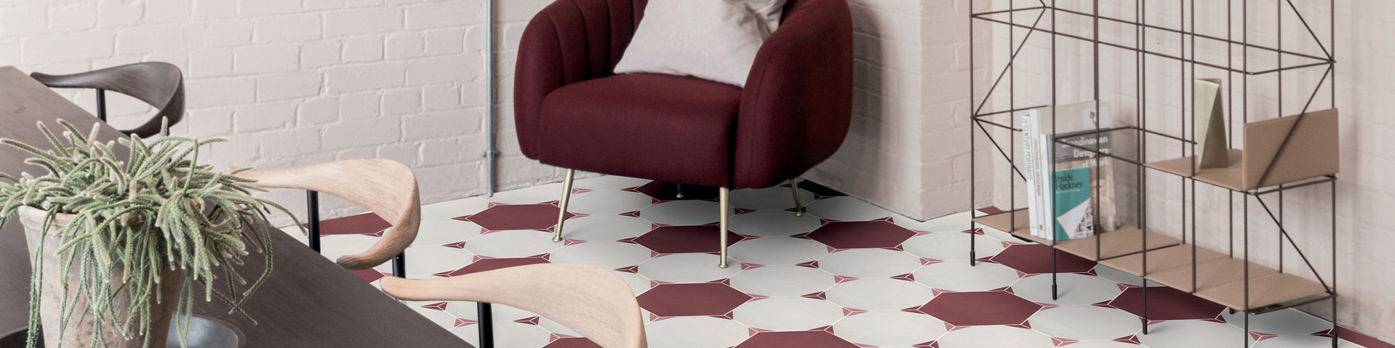 Meeting room with white and maroon hexagon floor tile, dark wood table, light wood chairs, maroon cushioned chair, and open shelving with potted plants.